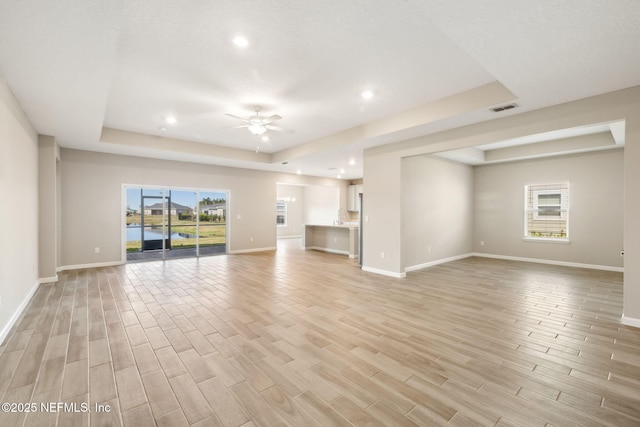 unfurnished living room featuring ceiling fan, a tray ceiling, and light wood-style flooring