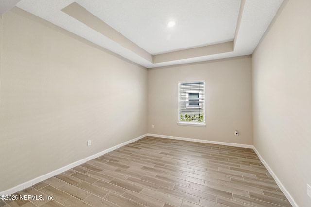 unfurnished room featuring baseboards, a tray ceiling, and wood finish floors