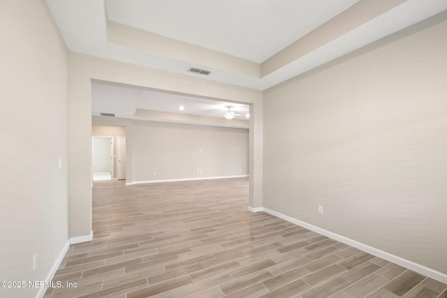 spare room with a tray ceiling, wood finish floors, visible vents, a ceiling fan, and baseboards