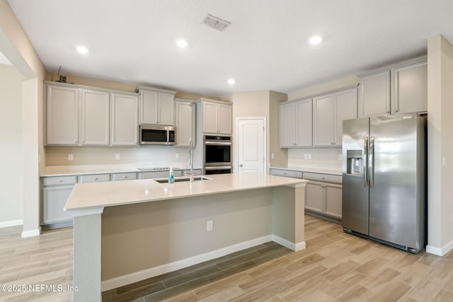 kitchen featuring an island with sink, gray cabinets, and stainless steel appliances