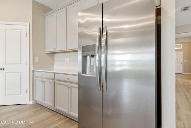 kitchen featuring light countertops, stainless steel fridge, visible vents, and light wood finished floors