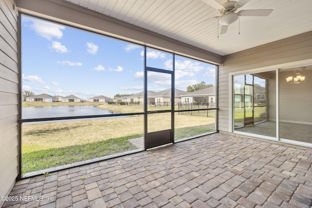 unfurnished sunroom featuring ceiling fan with notable chandelier, a water view, and a residential view