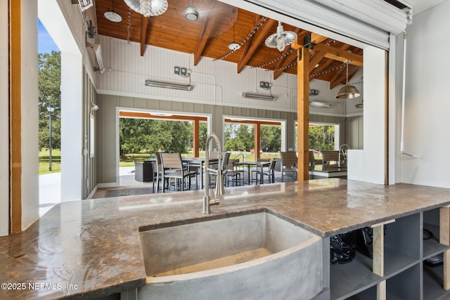 kitchen with stone counters, wood ceiling, a sink, and vaulted ceiling with beams