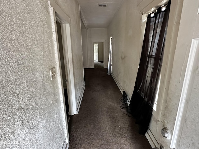 corridor featuring dark colored carpet, visible vents, and a textured wall