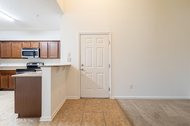 kitchen featuring appliances with stainless steel finishes, a peninsula, light tile patterned flooring, light countertops, and baseboards