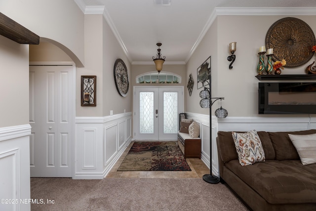 carpeted entryway with visible vents, arched walkways, a wainscoted wall, crown molding, and french doors