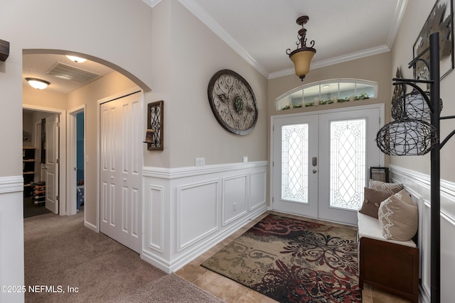 entryway featuring arched walkways, visible vents, french doors, ornamental molding, and wainscoting