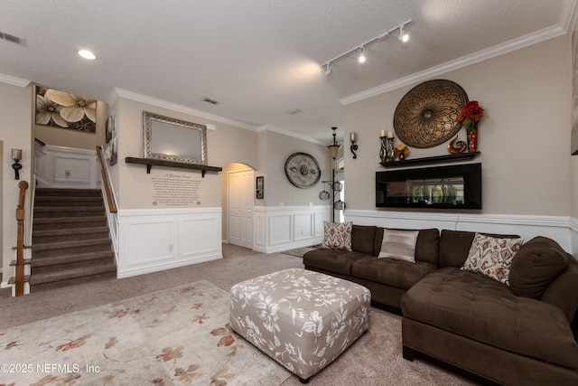 living room with light carpet, a wainscoted wall, rail lighting, stairs, and crown molding