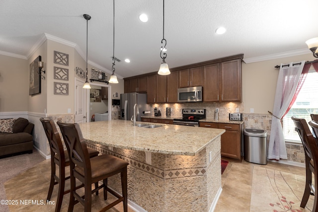 kitchen featuring a wainscoted wall, a breakfast bar area, appliances with stainless steel finishes, crown molding, and a sink