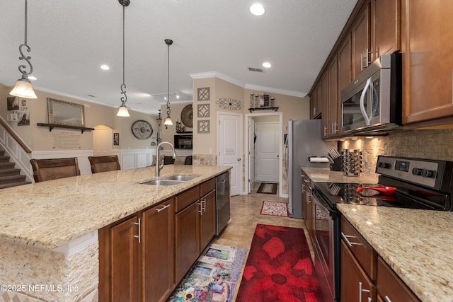 kitchen with crown molding, stainless steel appliances, visible vents, a sink, and an island with sink