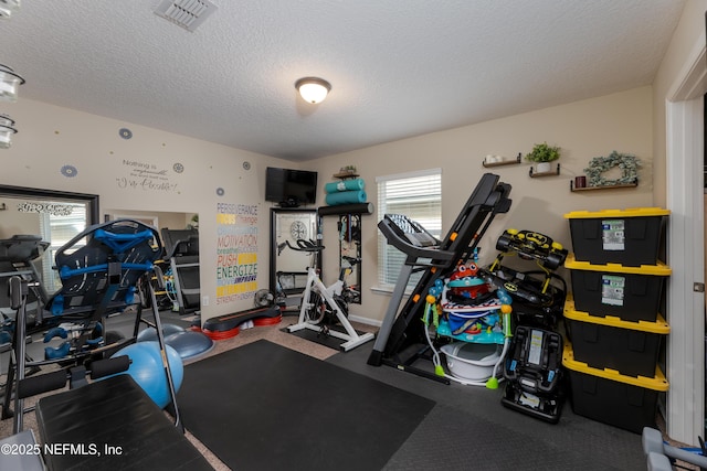 exercise area with baseboards, visible vents, and a textured ceiling