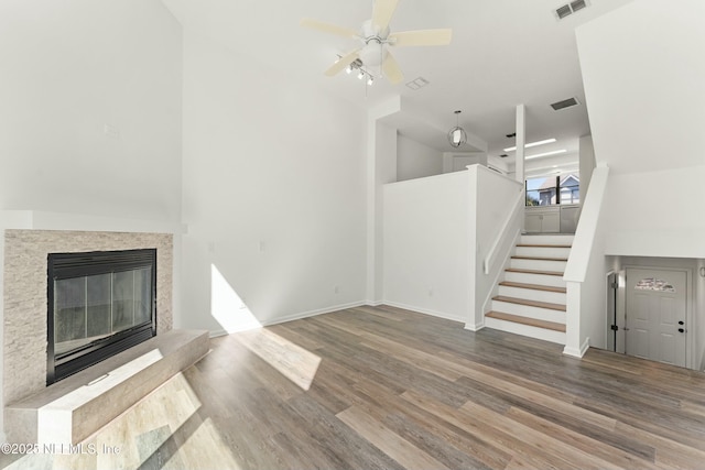 unfurnished living room featuring stairs, a glass covered fireplace, visible vents, and wood finished floors