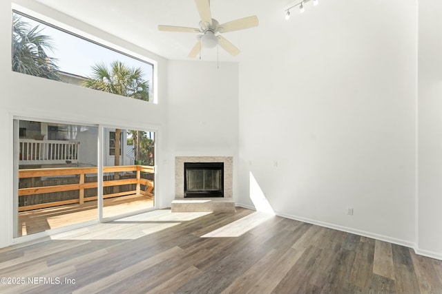 unfurnished living room featuring a ceiling fan, baseboards, wood finished floors, and a glass covered fireplace