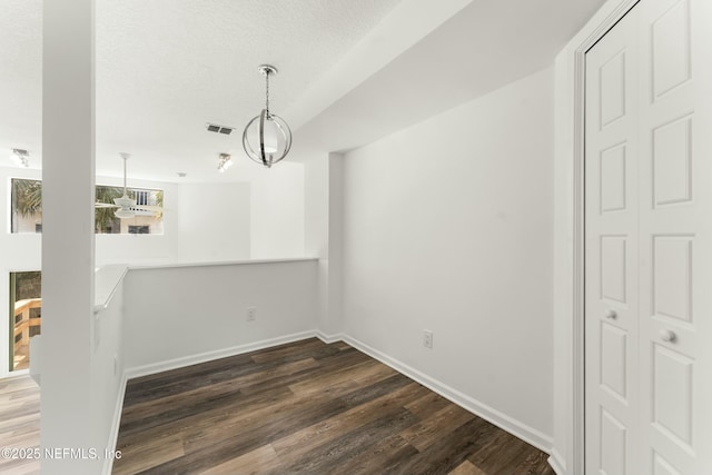 unfurnished dining area with dark wood-style flooring, visible vents, a textured ceiling, and baseboards