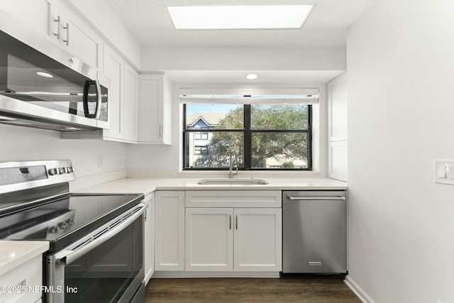 kitchen with dark wood finished floors, appliances with stainless steel finishes, light countertops, white cabinetry, and a sink