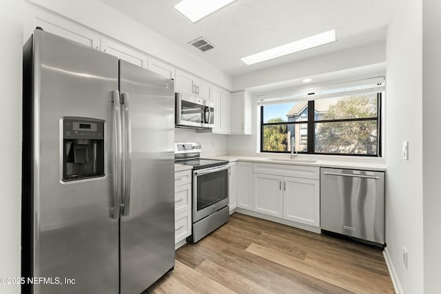 kitchen featuring stainless steel appliances, light countertops, visible vents, white cabinets, and a sink