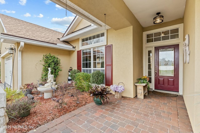 entrance to property with a garage, stucco siding, and roof with shingles