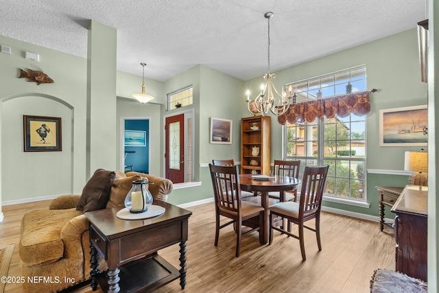 dining room featuring light wood-style floors, a notable chandelier, a textured ceiling, and baseboards