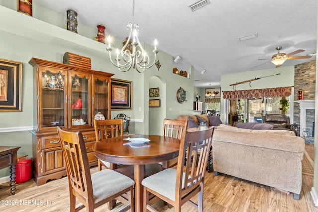 dining room with light wood finished floors, visible vents, arched walkways, and a textured ceiling