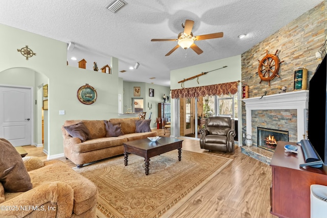 living area featuring visible vents, arched walkways, wood finished floors, a textured ceiling, and a stone fireplace