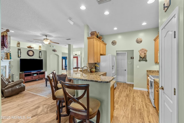 kitchen featuring white appliances, arched walkways, open floor plan, a peninsula, and light wood-type flooring