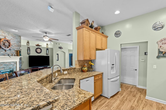 kitchen with arched walkways, light wood-style flooring, white appliances, a fireplace, and a sink