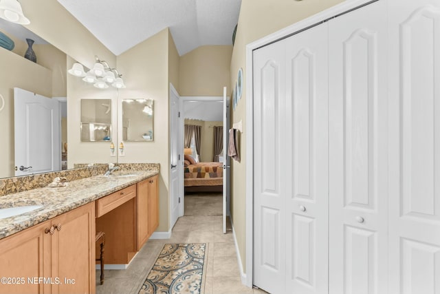 ensuite bathroom featuring a sink, vaulted ceiling, tile patterned floors, double vanity, and ensuite bath