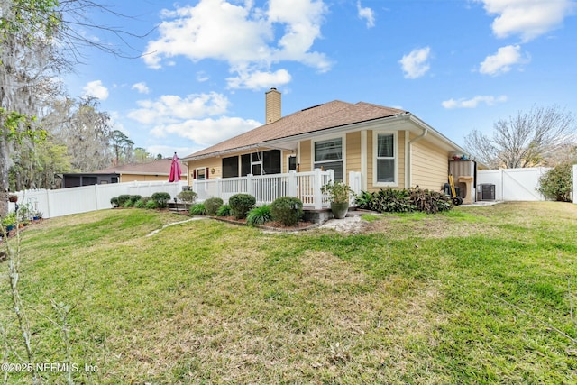 rear view of property featuring a fenced backyard, a chimney, a gate, and a lawn