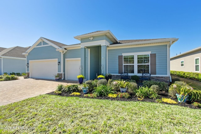 view of front of home with a garage, a front yard, stone siding, and decorative driveway