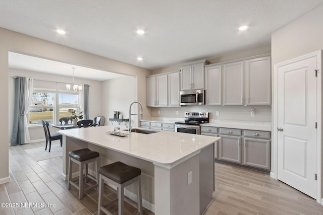 kitchen featuring a breakfast bar area, a sink, appliances with stainless steel finishes, gray cabinets, and wood tiled floor