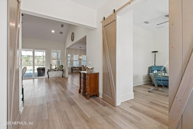 hallway featuring a barn door, visible vents, baseboards, lofted ceiling, and light wood-style flooring