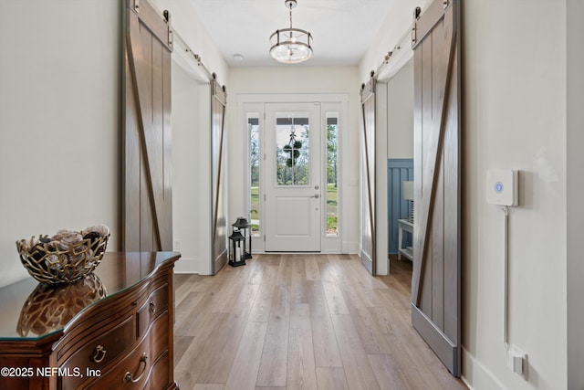 entryway with light wood-style flooring, baseboards, and a barn door