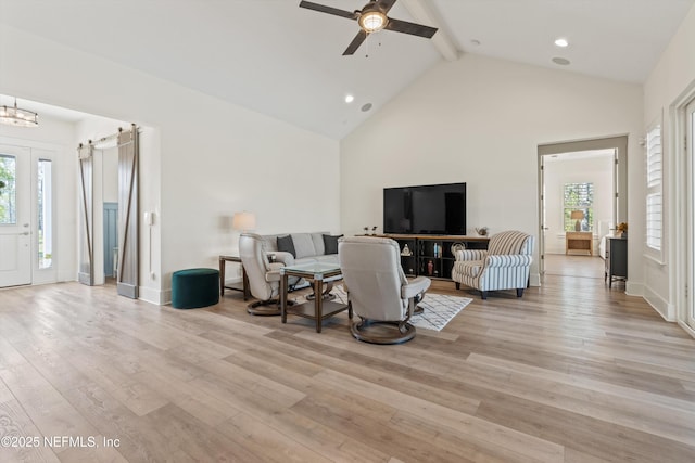 living area featuring high vaulted ceiling, a barn door, ceiling fan with notable chandelier, light wood-style floors, and beamed ceiling