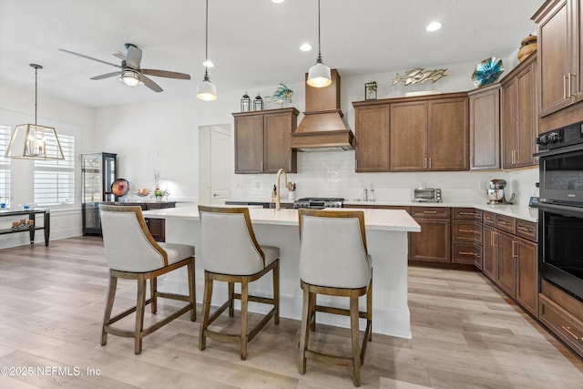 kitchen featuring dobule oven black, custom exhaust hood, light countertops, and a breakfast bar area