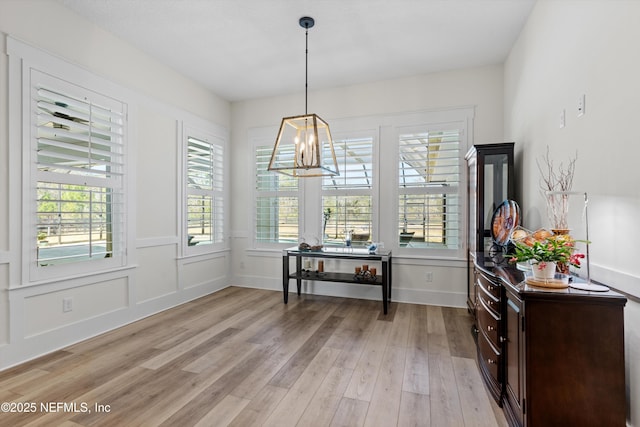 dining room with a chandelier, light wood finished floors, baseboards, and a decorative wall