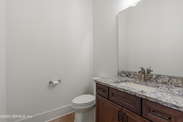 half bathroom with toilet, wood finished floors, vanity, and baseboards