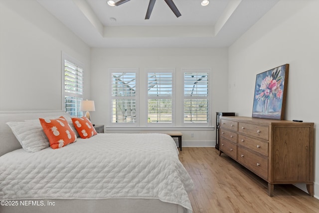 bedroom with a ceiling fan, a raised ceiling, light wood-style flooring, and baseboards