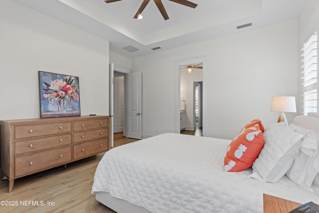 bedroom with light wood-type flooring, a tray ceiling, and visible vents