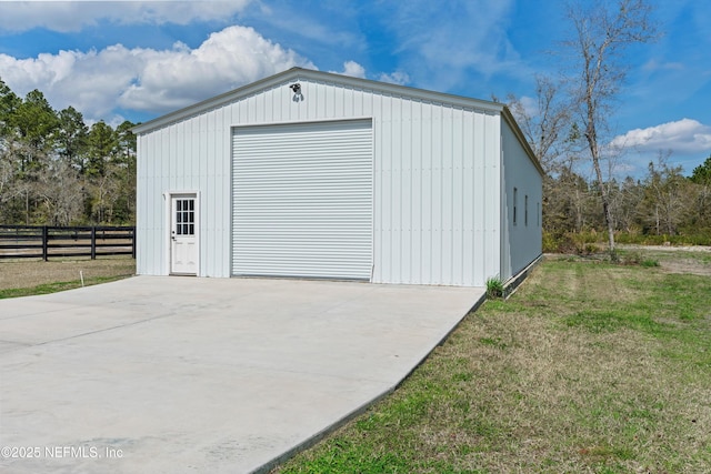 detached garage featuring concrete driveway and fence