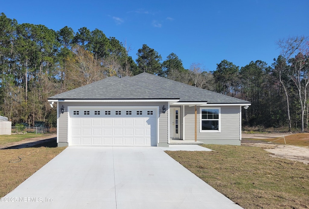 ranch-style home featuring driveway, an attached garage, a shingled roof, and a front yard