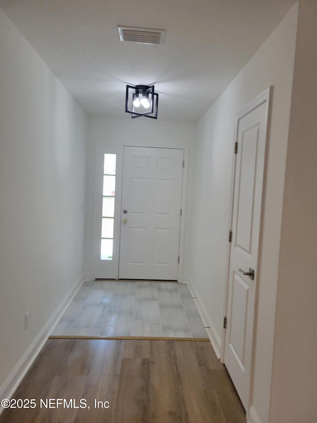foyer entrance featuring visible vents, a textured ceiling, baseboards, and wood finished floors