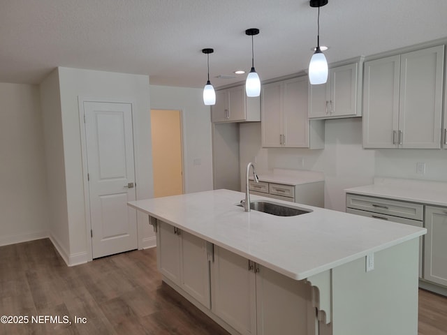 kitchen featuring a sink, decorative light fixtures, an island with sink, gray cabinets, and dark wood-style flooring