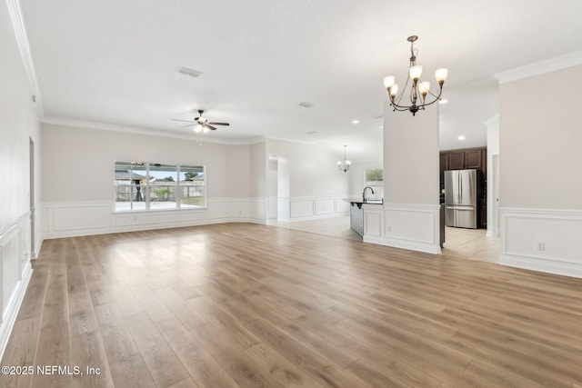 unfurnished living room with light wood-type flooring, a wealth of natural light, crown molding, and ceiling fan with notable chandelier