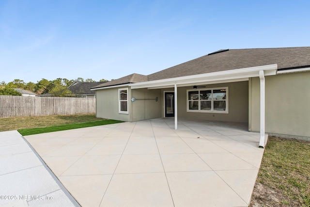 back of house with a shingled roof, a patio, ceiling fan, fence, and stucco siding