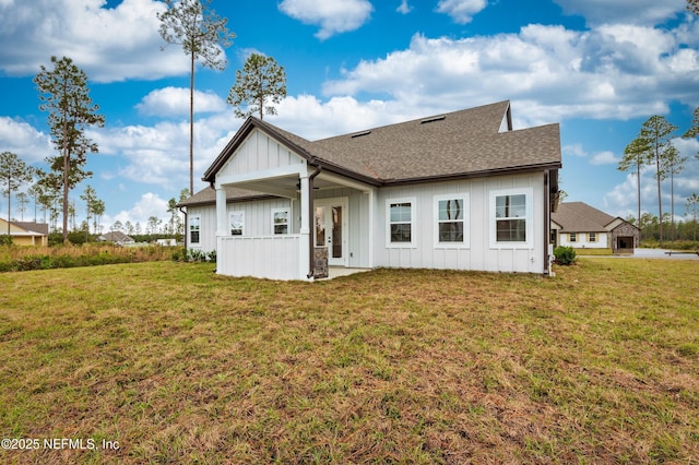 rear view of house with ceiling fan, roof with shingles, board and batten siding, and a lawn