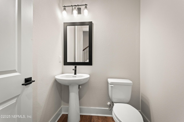 half bathroom with baseboards, a sink, toilet, and wood finished floors