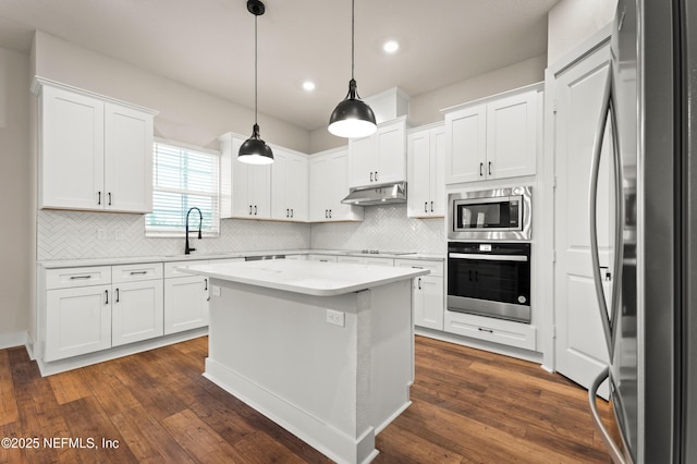 kitchen featuring dark wood-type flooring, stainless steel appliances, light countertops, under cabinet range hood, and a sink