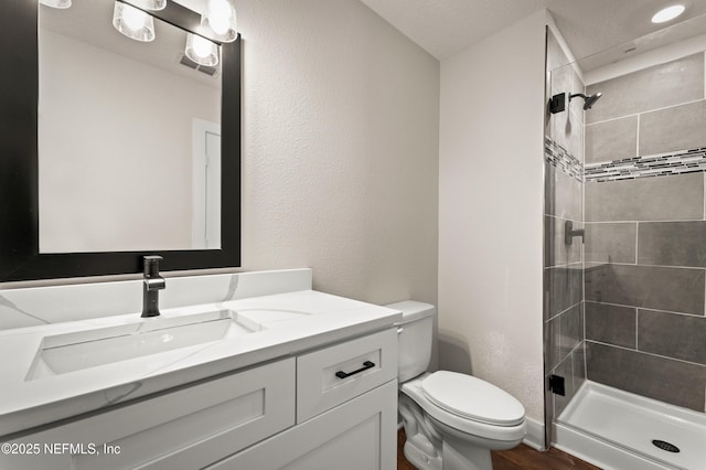 bathroom featuring a textured wall, toilet, wood finished floors, vanity, and a shower stall