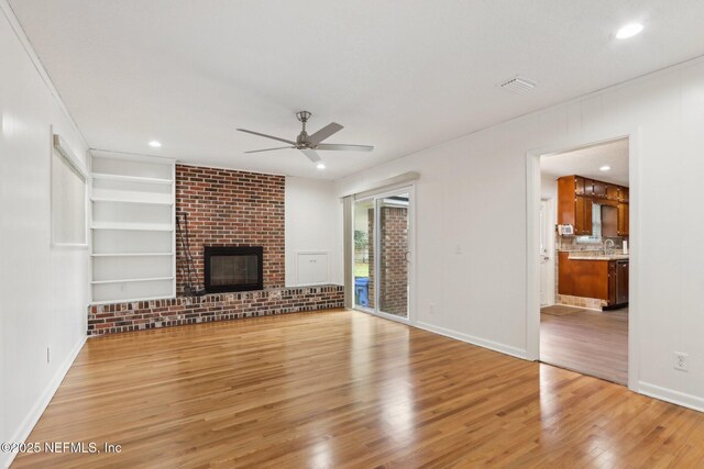 unfurnished living room featuring built in shelves, baseboards, a fireplace, ceiling fan, and light wood-style floors
