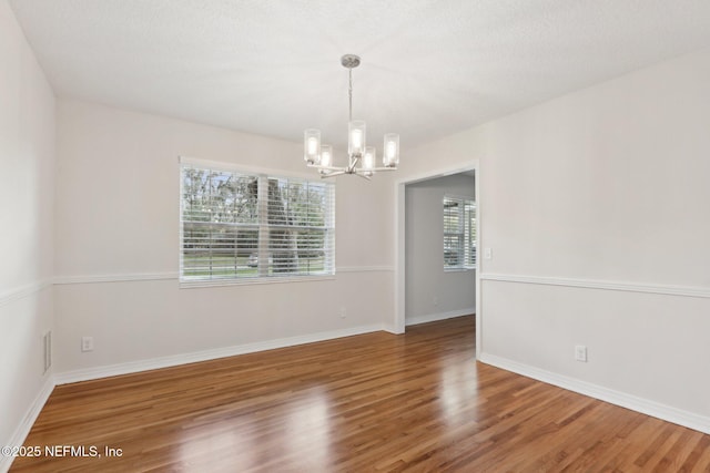 spare room featuring visible vents, baseboards, an inviting chandelier, and wood finished floors